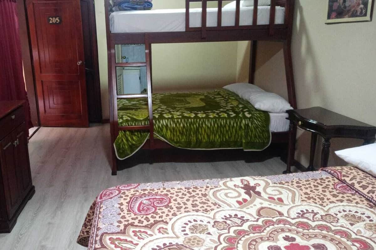 Um quarto com uma cama de solteiro e beliche, um armário de madeira, uma televisão e um cobreleiro estampado.