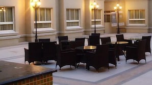 Uma área externa com mesas e cadeiras, cercada por um edifício com várias janelas e piso de azulejos.