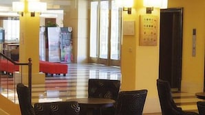 Um hall de hotel com áreas de estar, um balcão de recepção e uma escadaria que dá acesso a outros andares.