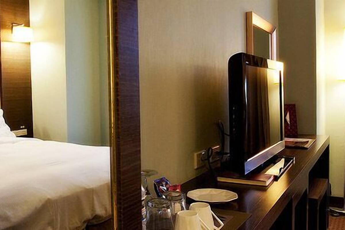Een hotelkamer met een bed, een bureau met een flatscreen televisie, een spiegel en een lamp.