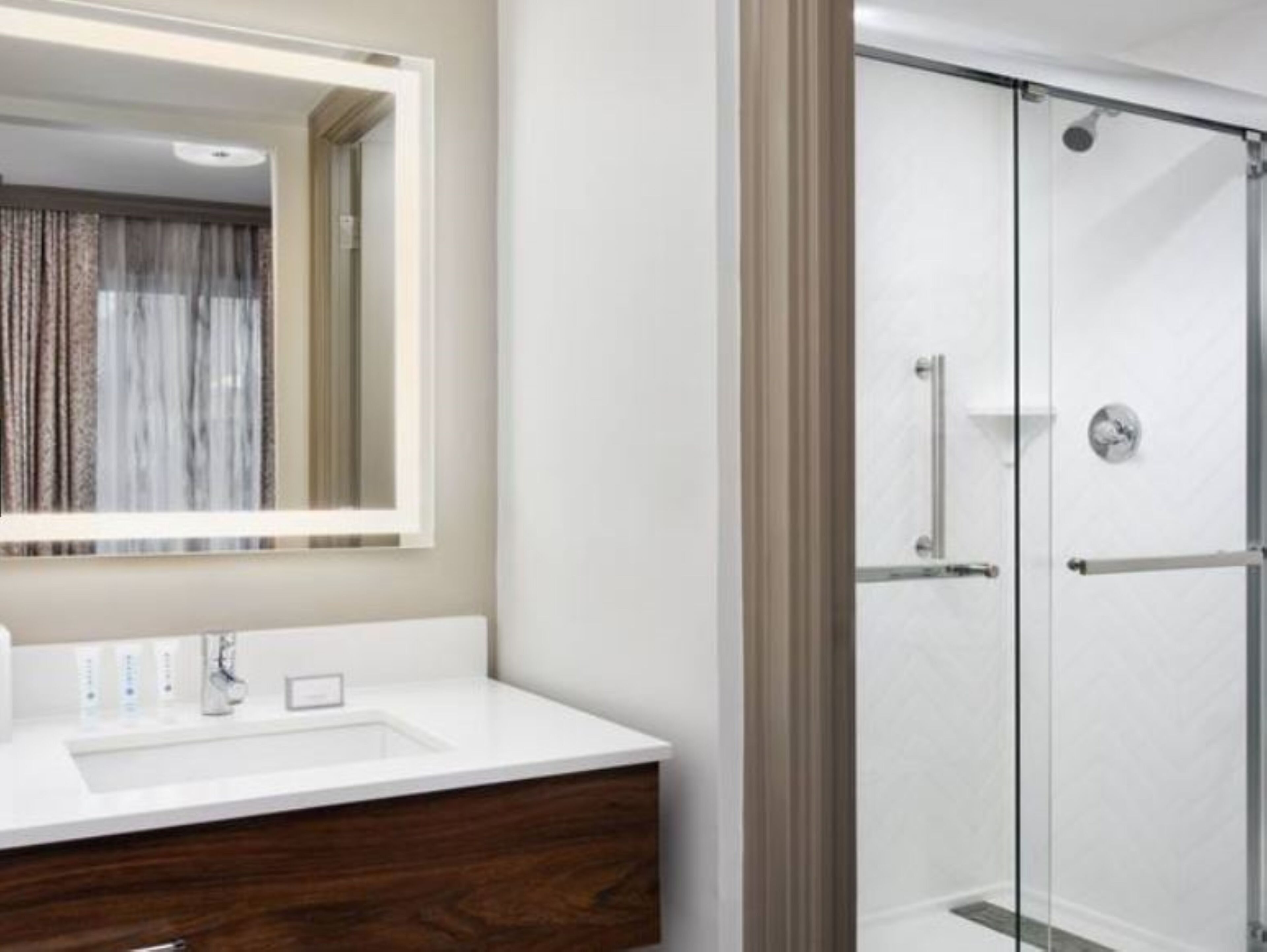 A modern bathroom with a large mirror, a white sink, and a glass shower enclosure.