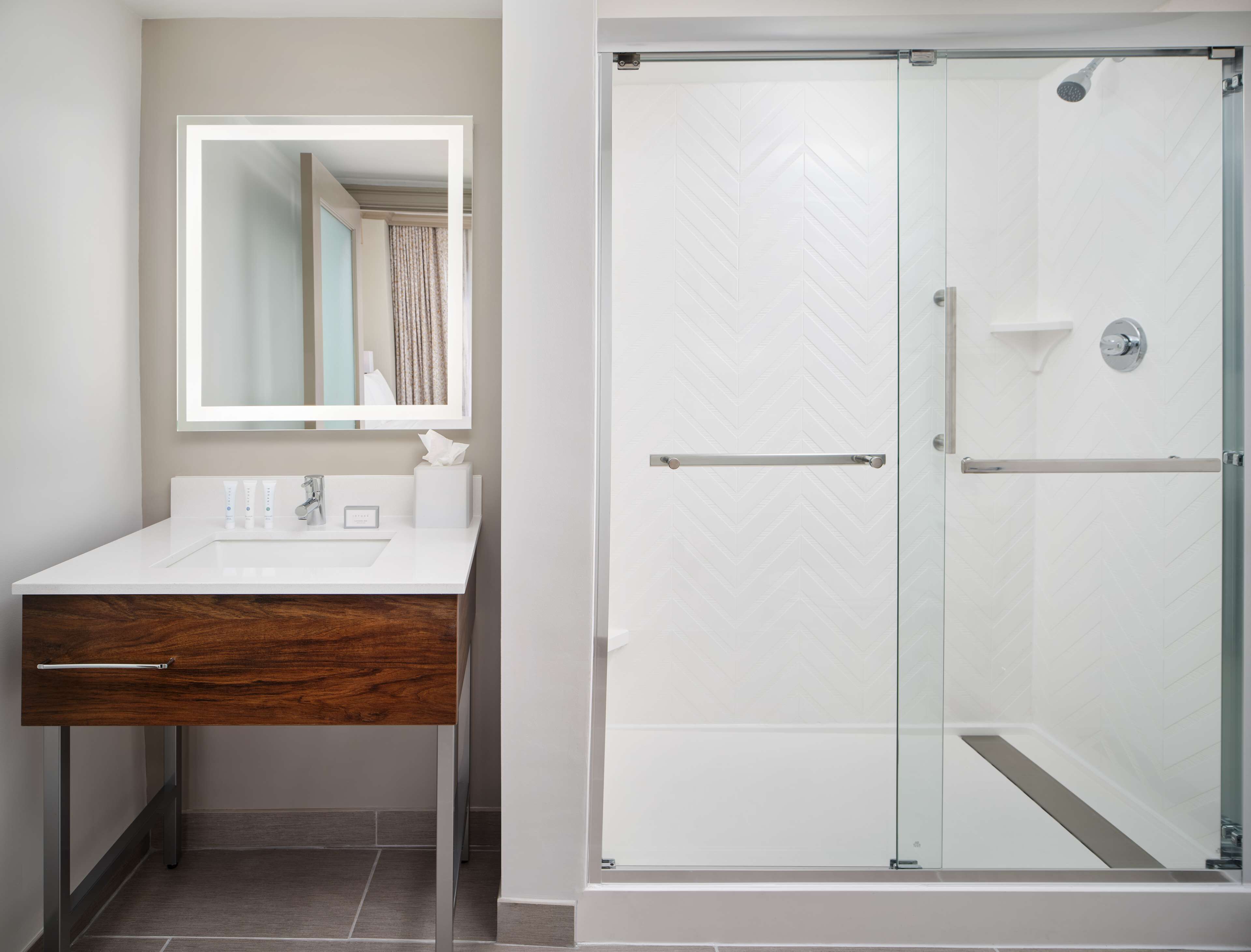 A modern bathroom with a white vanity, a mirror, and a glass-enclosed shower.