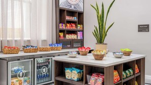 Una tienda de dulces y bebidas, una planta en maceta, y un letrero que indica que está abierta las 24 horas.