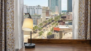 Vista desde una ventana con cortinas, que incluye una lámpara, un paisaje urbano con edificios y palmeras.