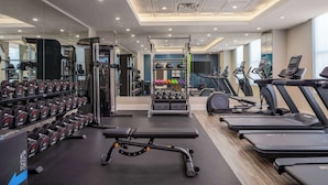 Un gimnasio moderno con diversos equipos, incluyendo mancuernas, máquinas de pesas, cintas de correr y una banca.