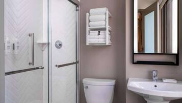 A bathroom with a glass shower enclosure, a white toilet, a sink with a mirror above it, and a towel rack with folded towels.