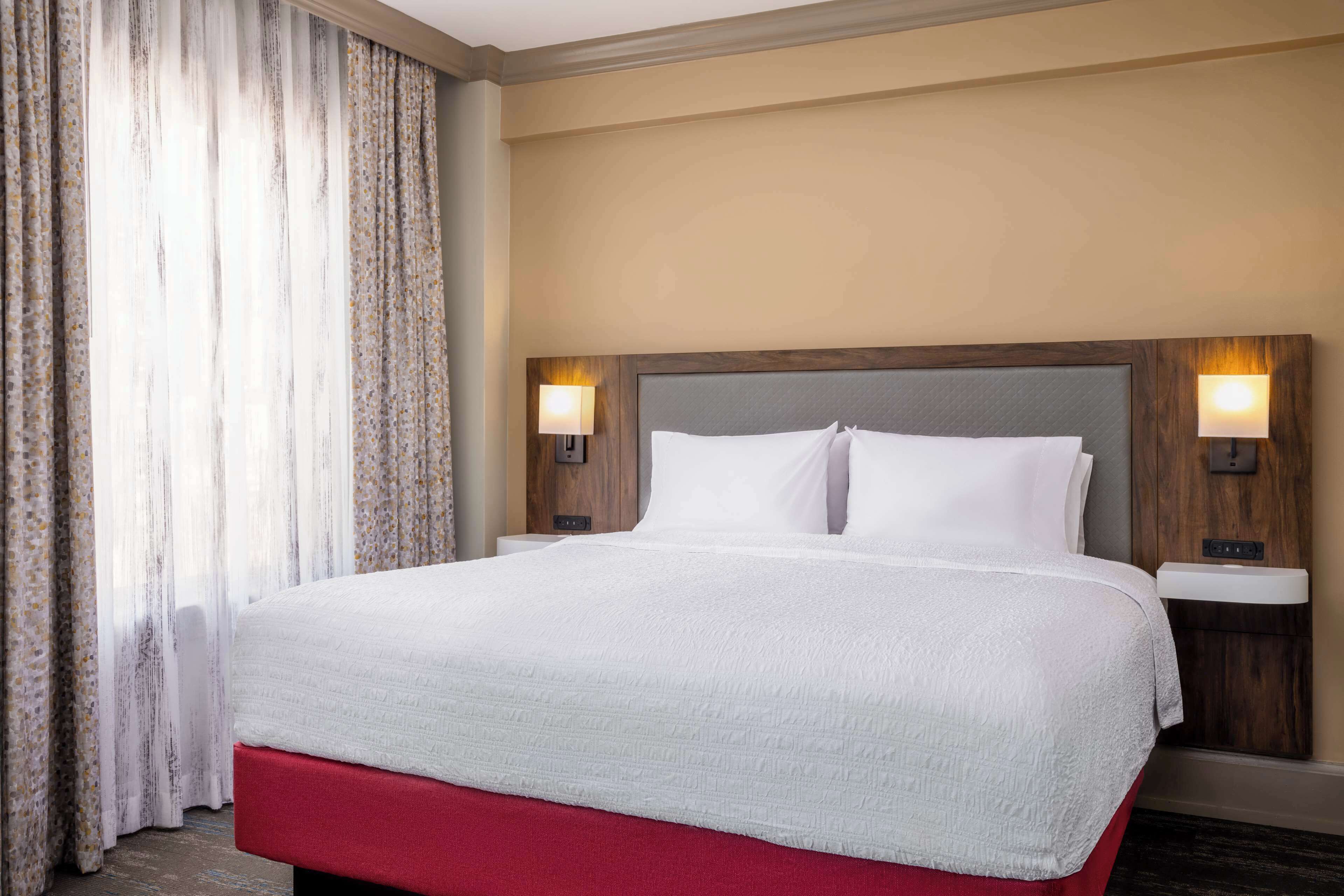 A hotel room with a large bed, two bedside lamps, and a window with curtains.