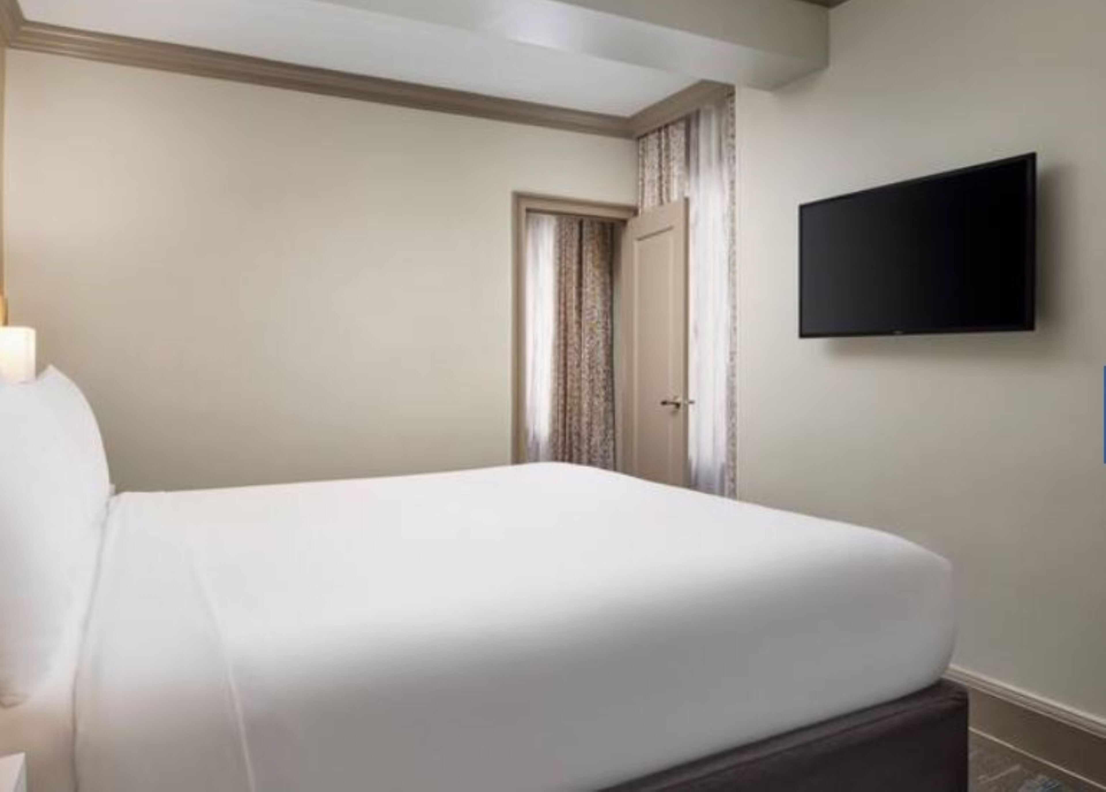 Habitación de hotel con una cama grande, televisor de pantalla plana montado en la pared y una puerta con cortinas.