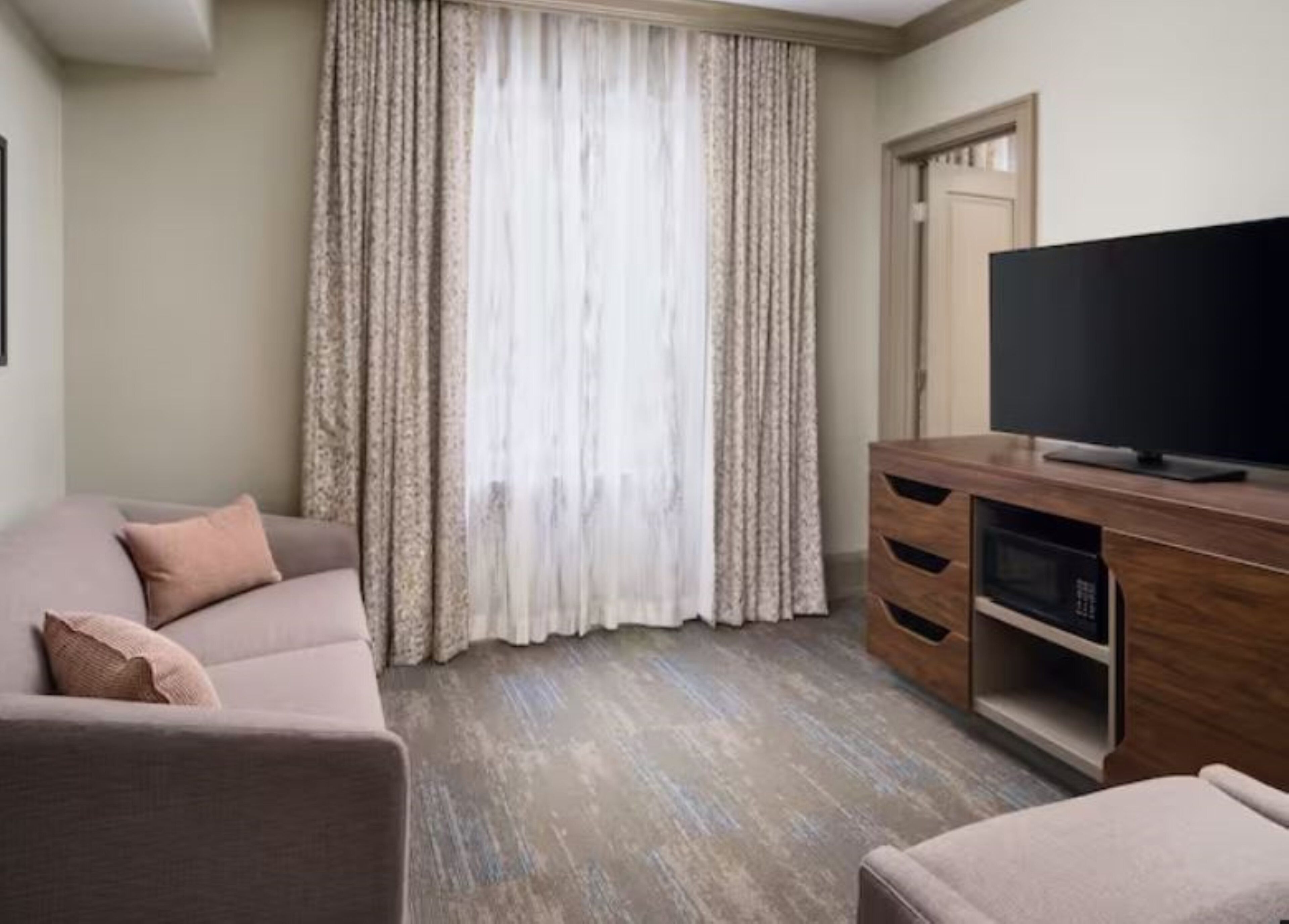 A living room with a sofa, a television on a wooden cabinet, and a window with curtains.