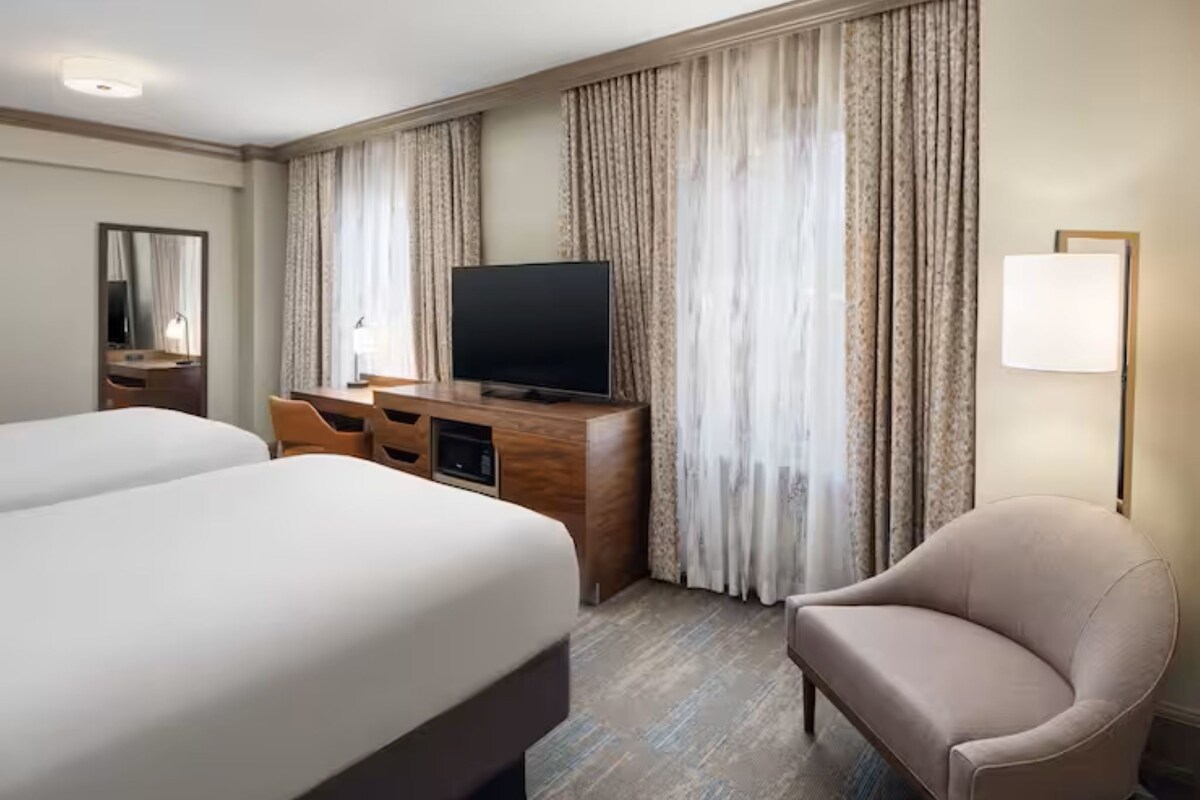 A hotel room with two beds, a TV, a desk, and a chair.