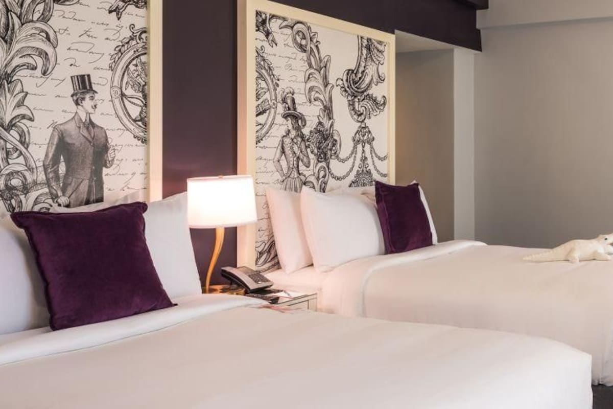 A hotel room with two beds, a desk, a chair, and a TV.