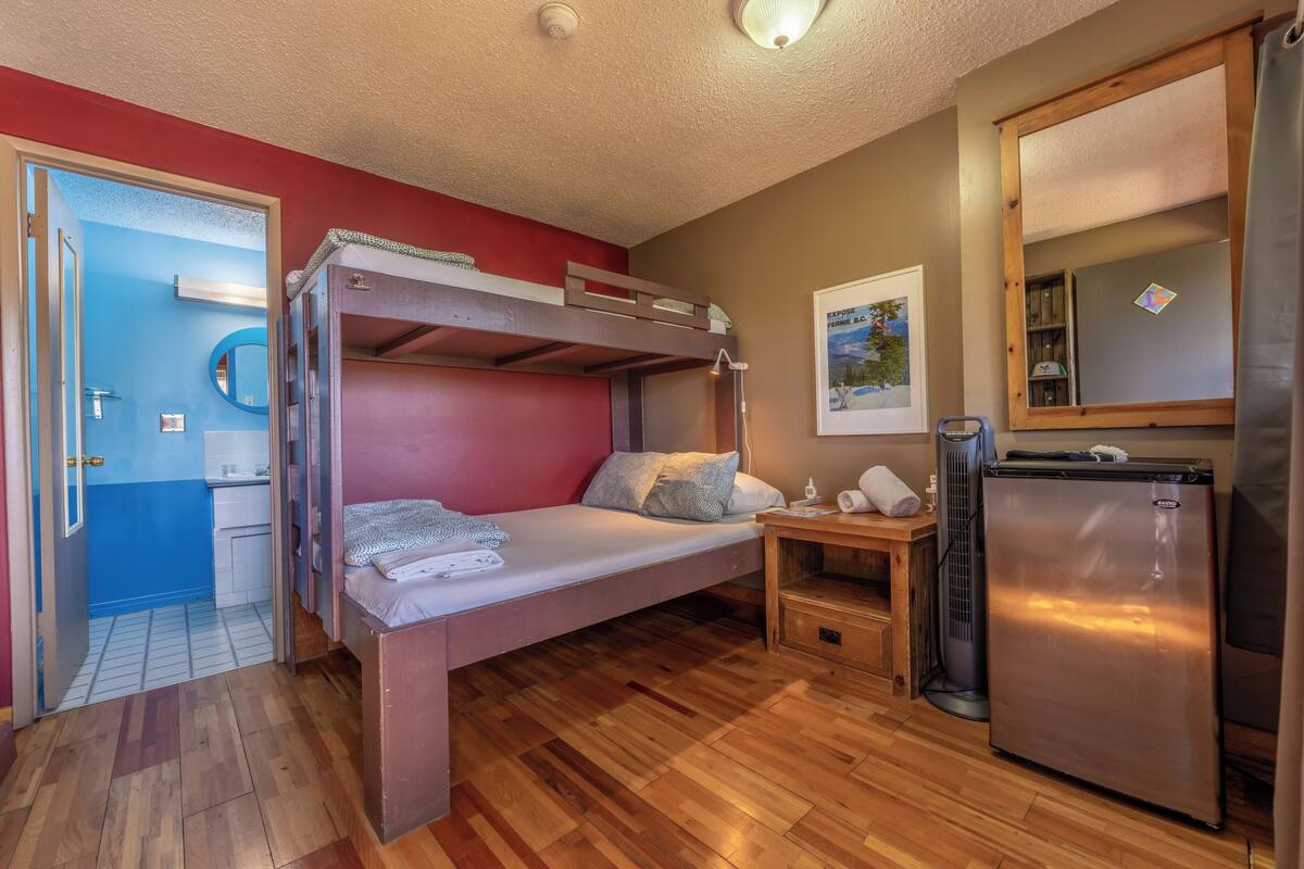 Una cama individual con escritorio y refrigerador en una habitación con piso de madera y una puerta azul.