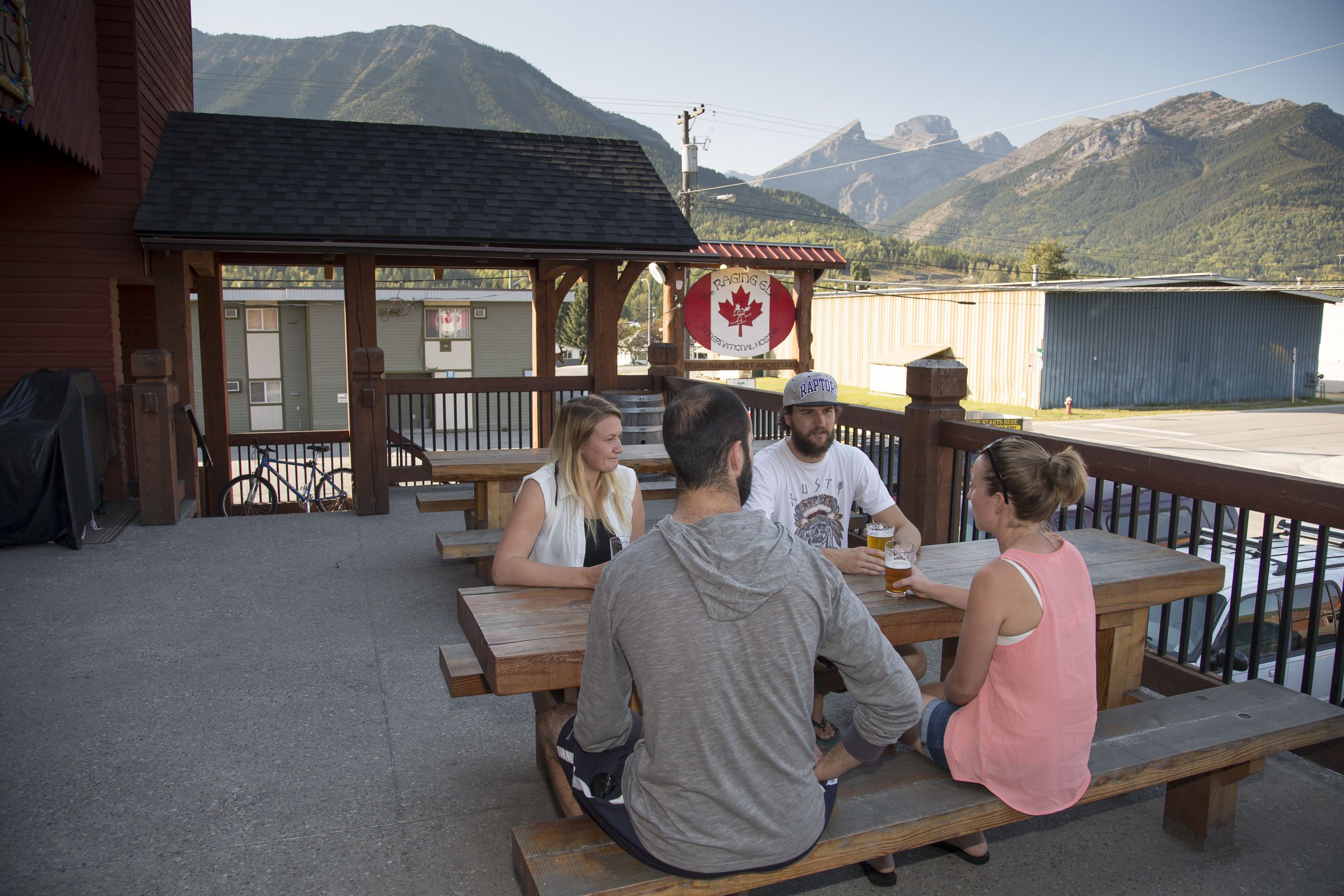 A group of people seated at wooden picnic tables outdoors with a mountain backdrop.