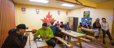 Un groupe de personnes est assis à des tables de pique-nique en bois dans une pièce aux murs jaunes, décorée d’une grande feuille d’érable rouge.
