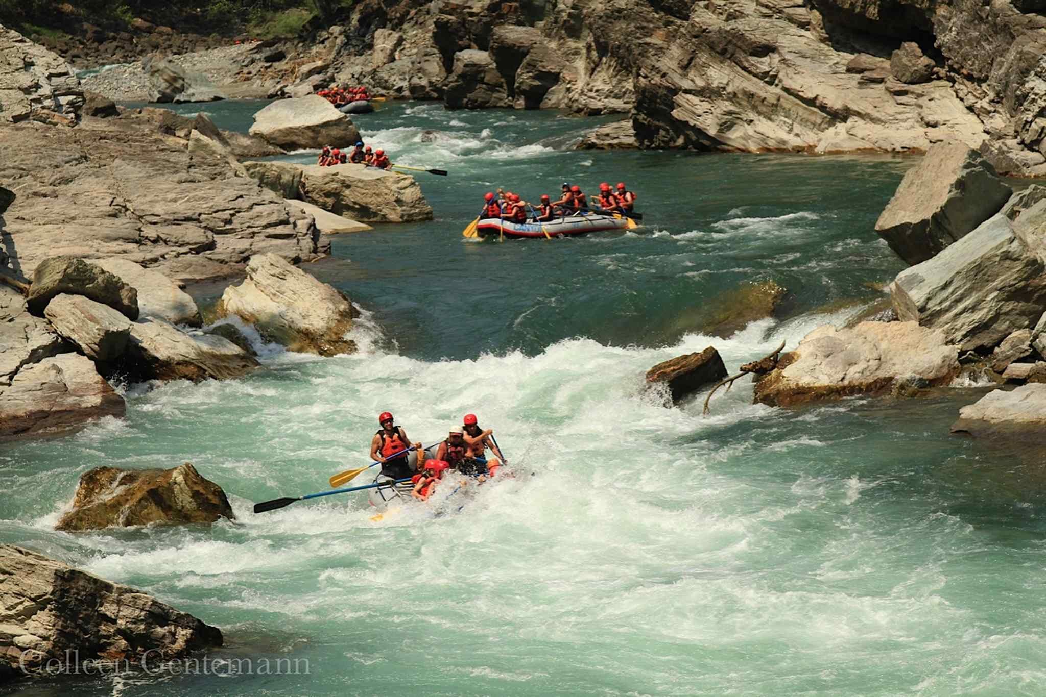 Un grupo de personas haciendo rafting en un río rodeado de terreno rocoso.