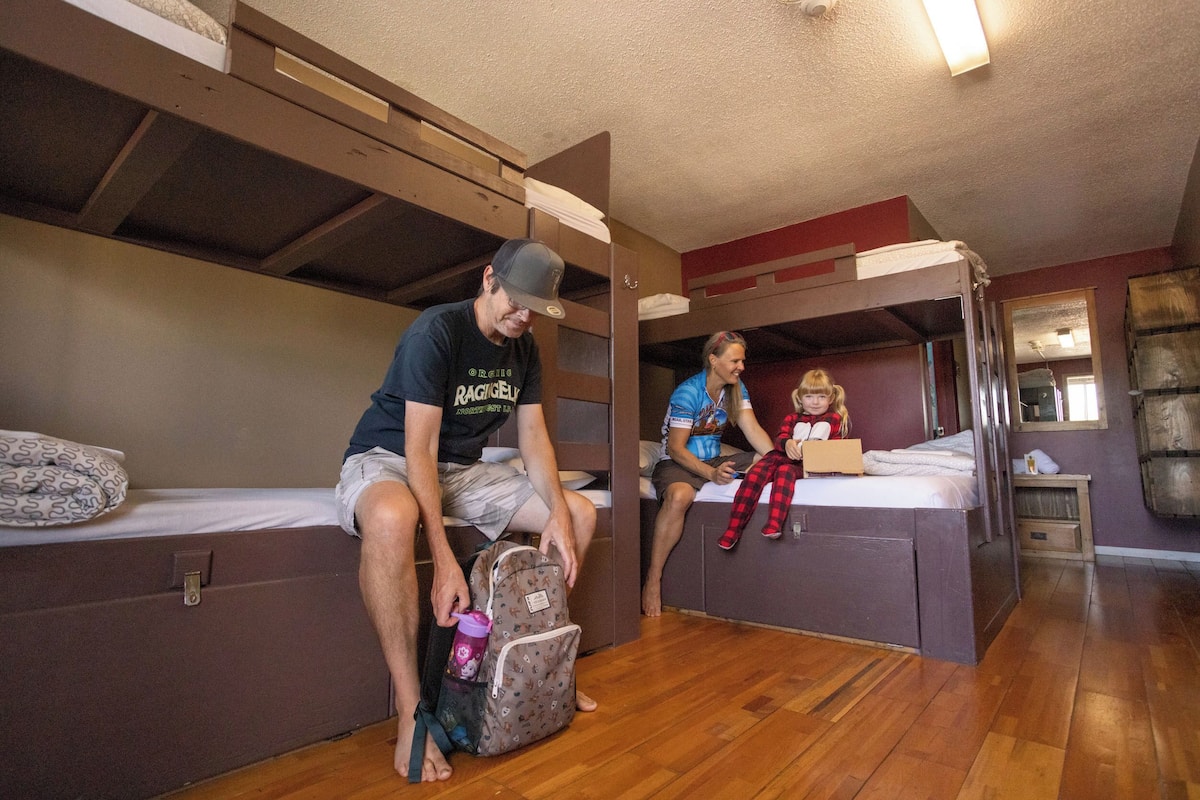 Una habitación con literas, piso de madera y una pequeña mesa con una silla.