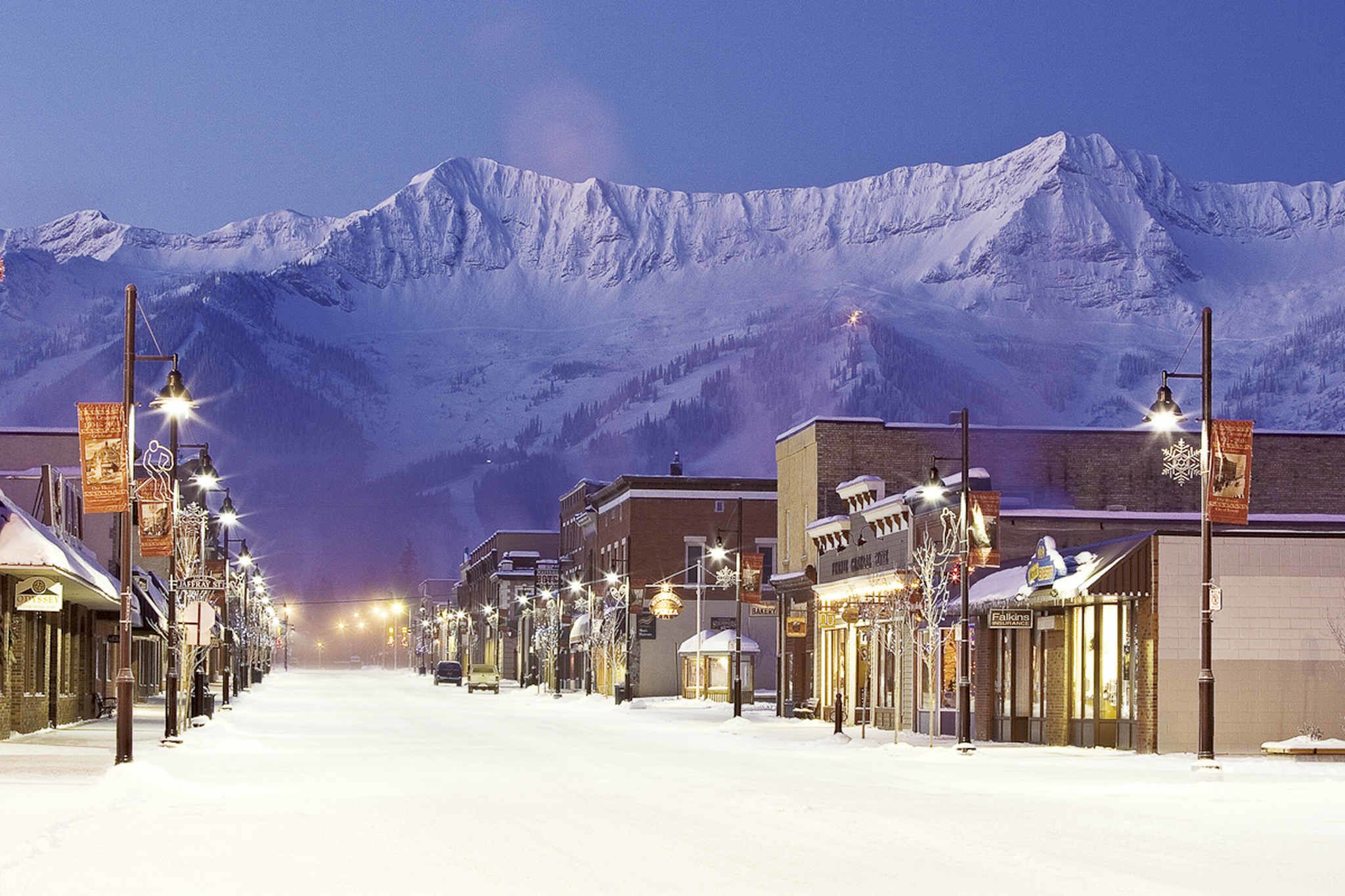 Une rue enneigée, avec des bâtiments et une montagne en arrière-plan.