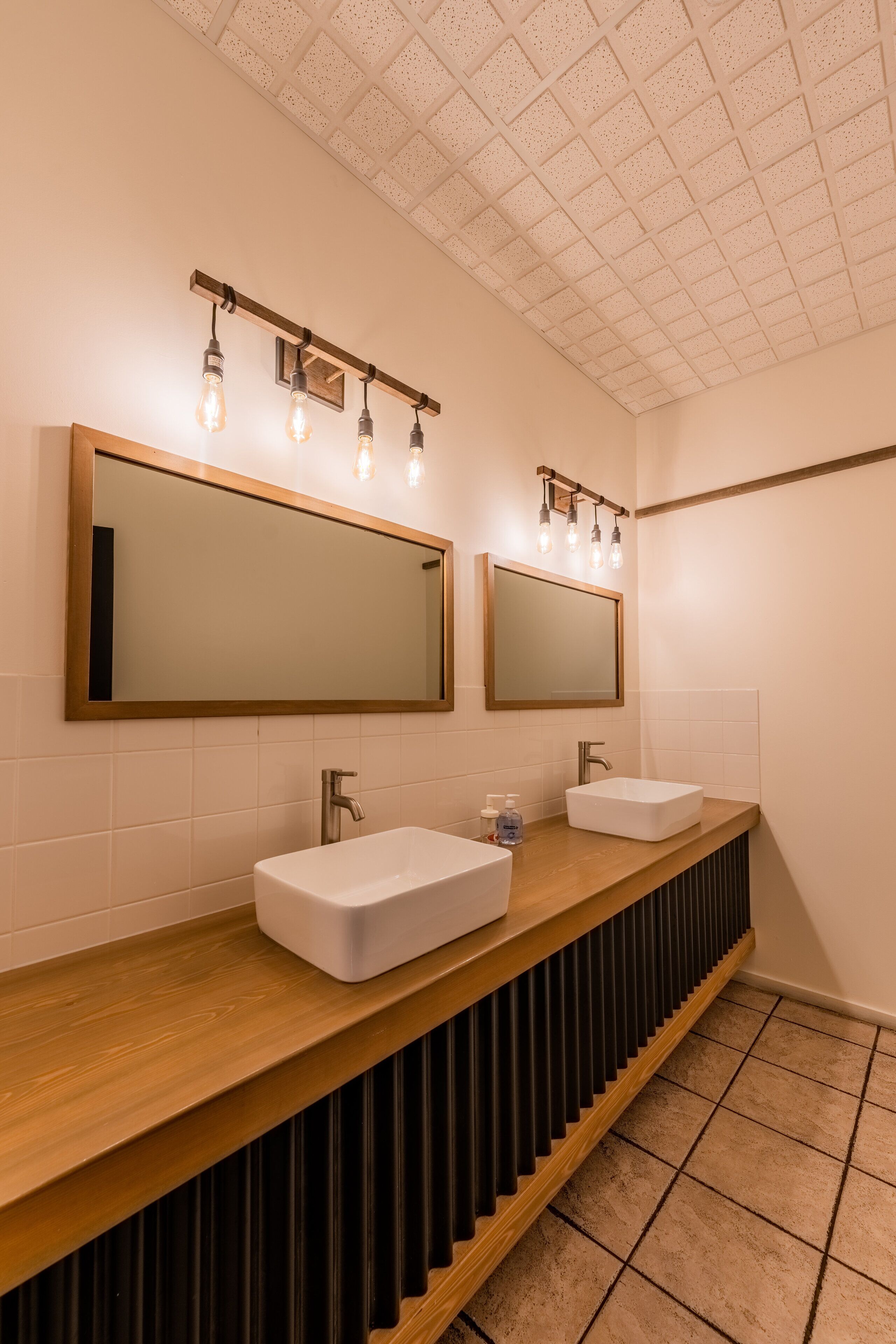 A modern bathroom with two sinks, a wooden vanity, and a ceiling with a grid pattern.