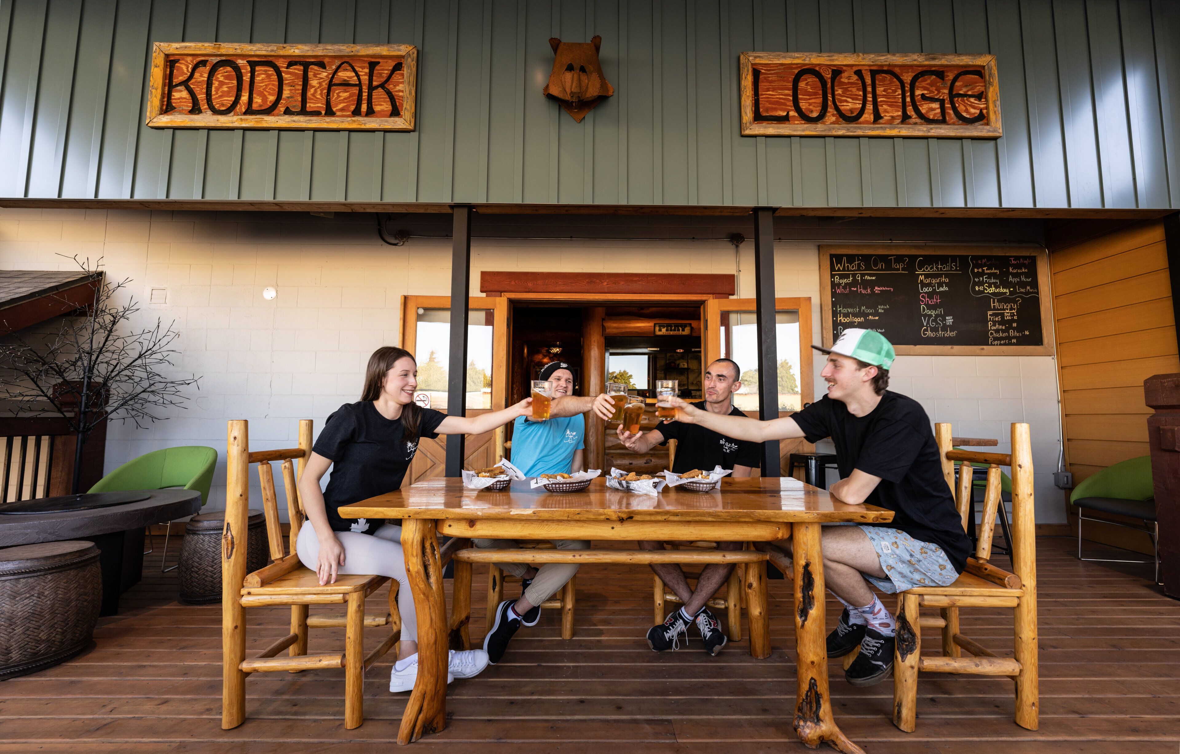 Ein Holztisch mit vier Stühlen in rustikaler Umgebung, eine Speisekarte und ein Schild mit der Aufschrift 'KODTAK LOUNGE'.