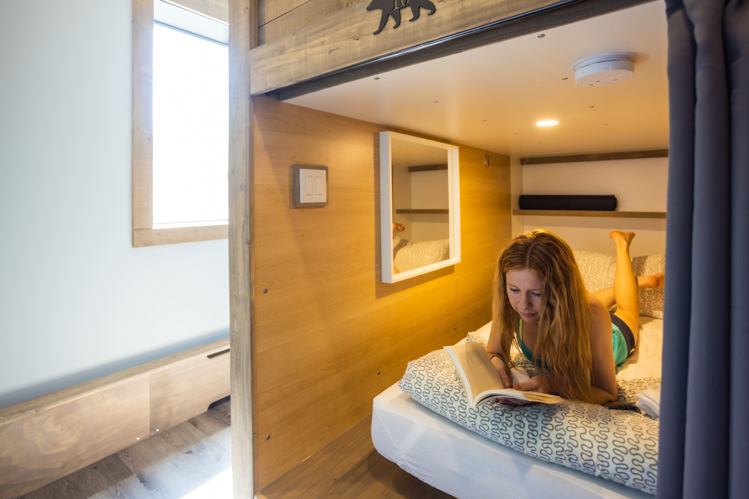 A room with a bed, a window, and a mirror on the wall.