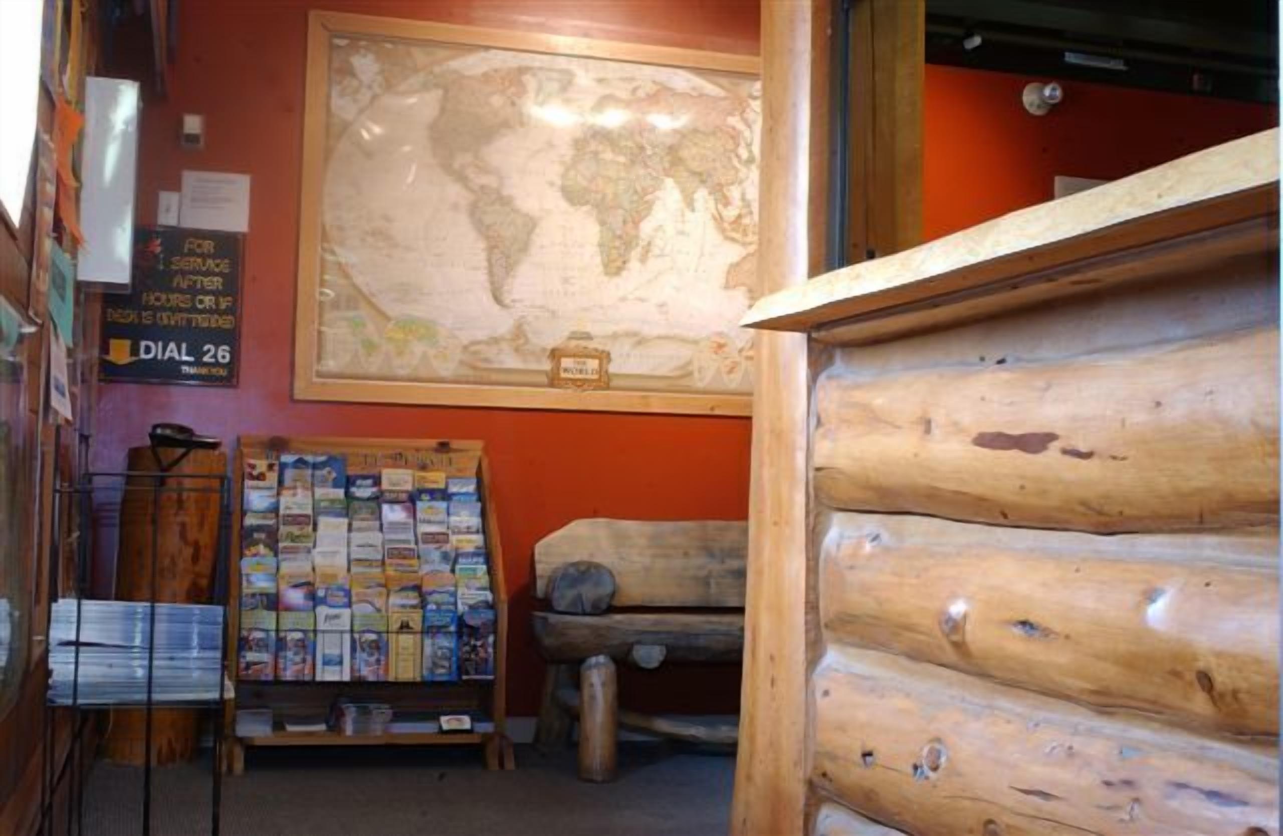 A cabin interior with a wooden log wall, a world map on the wall, and a bulletin board with various items.