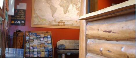 A cabin interior with a wooden log wall, a world map on the wall, and a bulletin board with various items.
