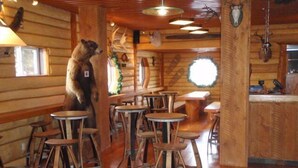 A rustic wooden interior with a pool table, wooden stools, and antler decorations.