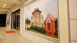 Un pasillo con un cuadro enmarcado de un edificio tradicional y una estructura roja, posiblemente un pagode, en un entorno hotelero.