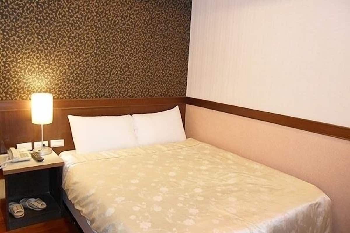 Una habitación de hotel con una cama, una mesita de noche con lámpara y un teléfono.