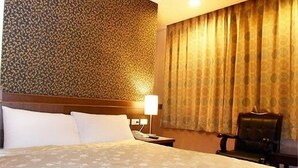 Habitación de hotel con una cama grande, cabecera, mesita de noche con lámpara, una silla y pared con diseño.