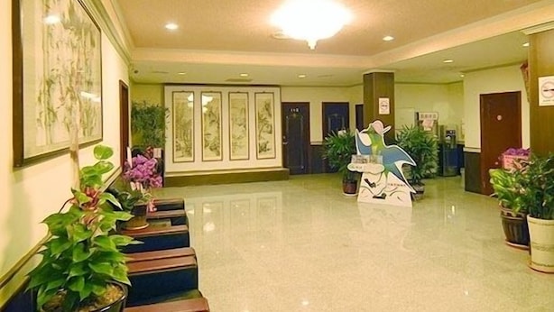 Un vestíbulo de hotel con una recepción, obras de arte enmarcadas en las paredes y plantas en macetas.