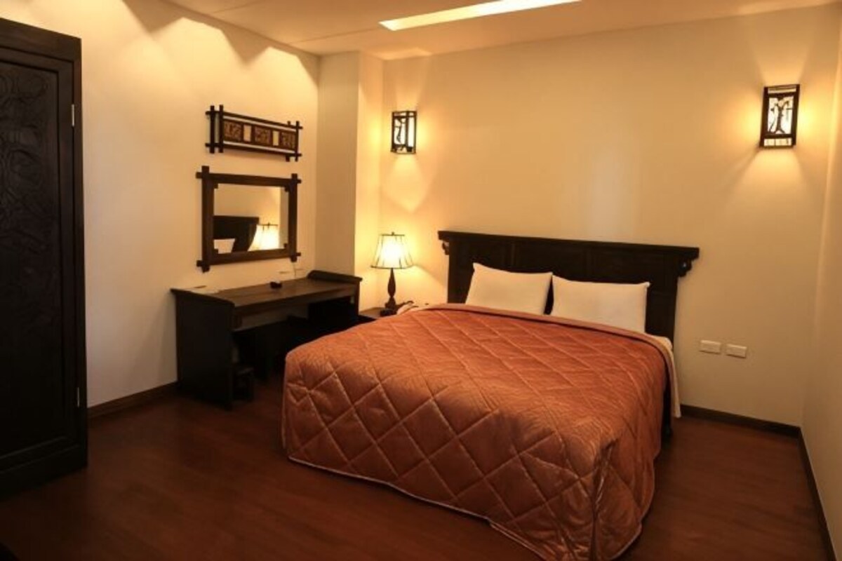 A bedroom with a bed, a desk, a mirror, and wall-mounted lights.
