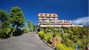 A multi-story hotel with a red roof and balconies, surrounded by greenery and a clear sky. - Chun Jing Hillview Villa (Ren'ai)