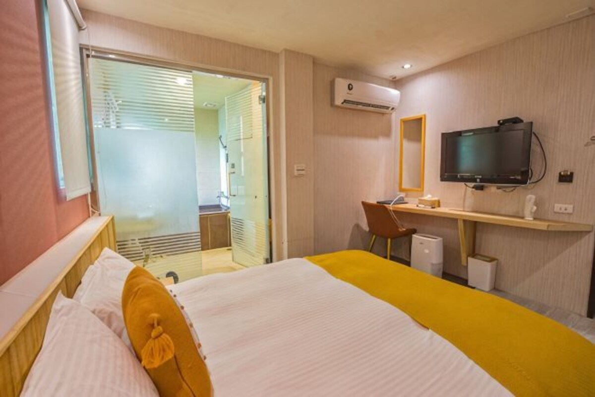 A hotel room with a bed, a desk, a chair, a television, and an air conditioning unit.