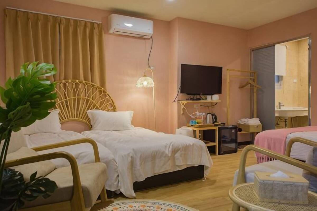 Ein Hotelzimmer mit zwei Betten, einem Fernseher, einem Nachttisch, einer Pflanze und einem Fenster mit Vorhängen.
