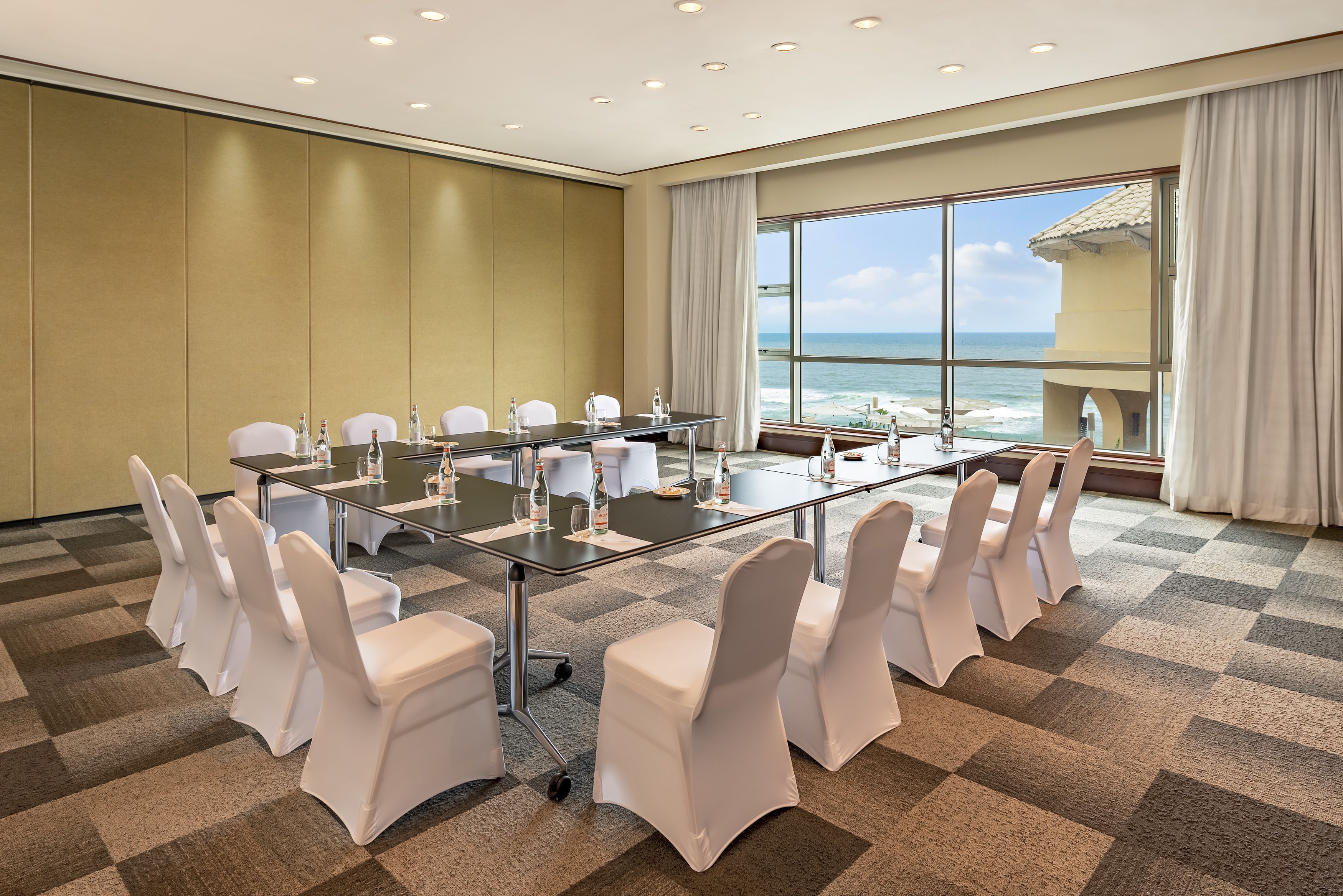 A conference room with a large table, white chairs, and a view of the ocean.