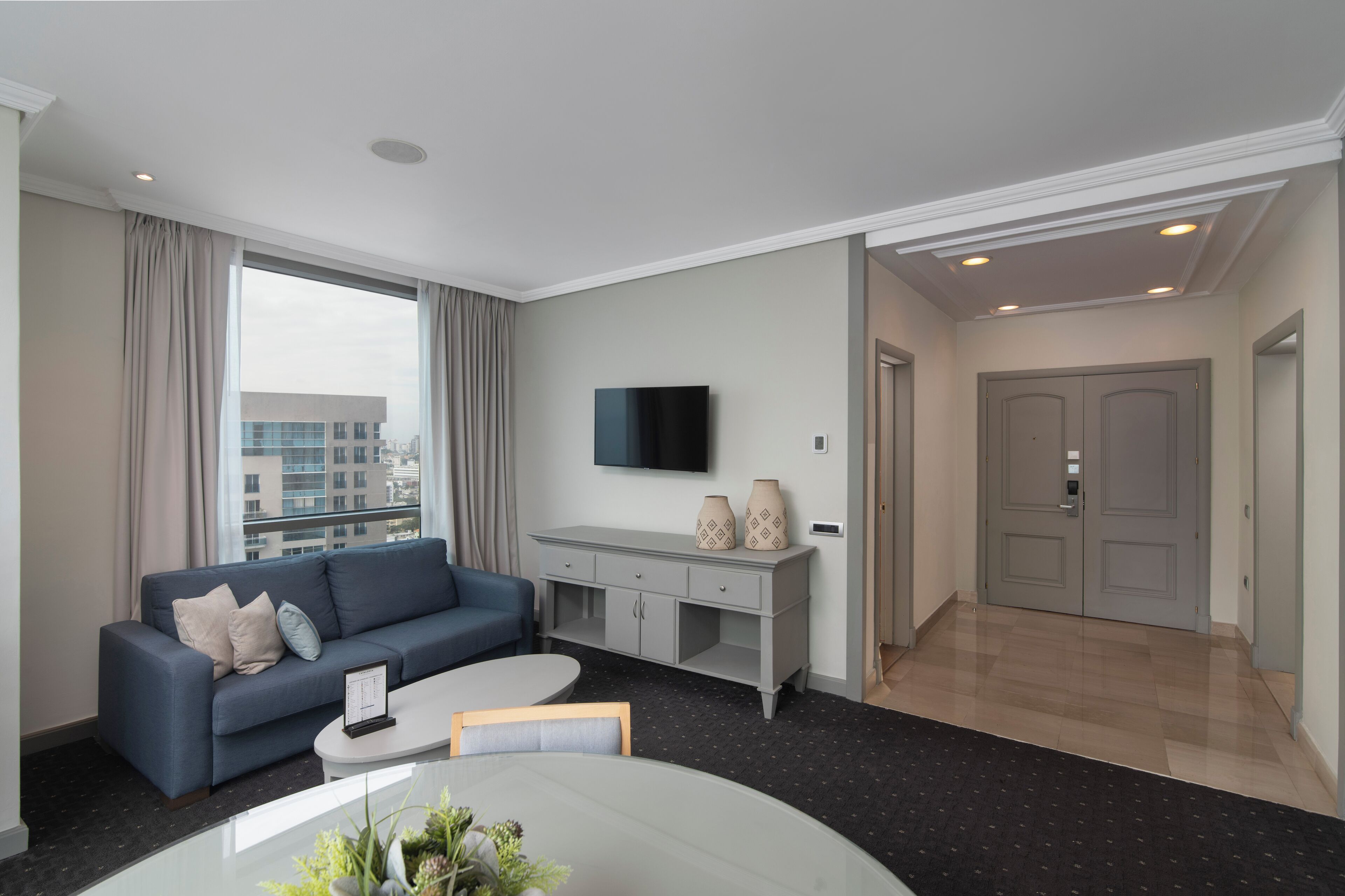 Una sala de estar moderna con un sofá azul, una mesa de centro, un televisor de pantalla plana y un mueble bajo en gris.