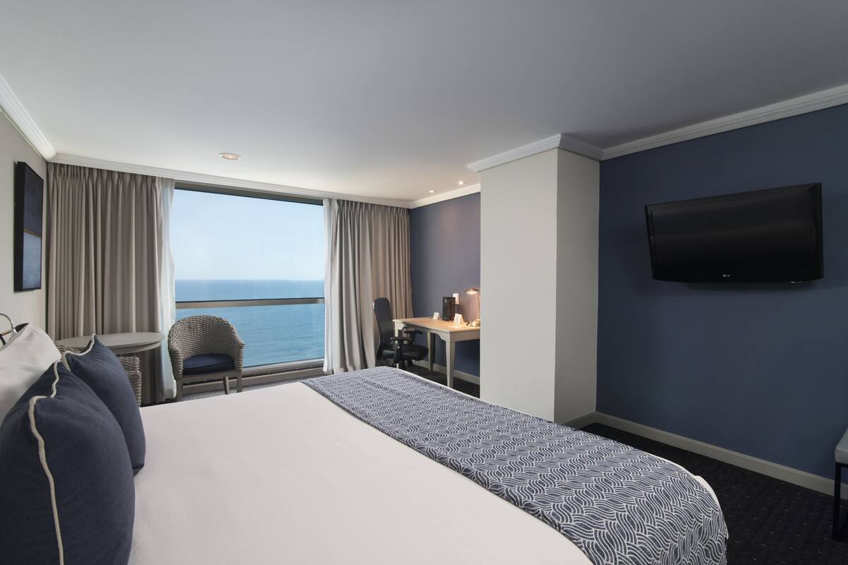 Une chambre d’hôtel avec un grand lit, un bureau, une chaise, une télévision et une vue sur la mer.
