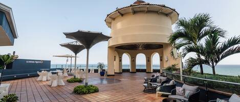 A rooftop terrace with outdoor seating, a central decorative structure, and a view of the sea.