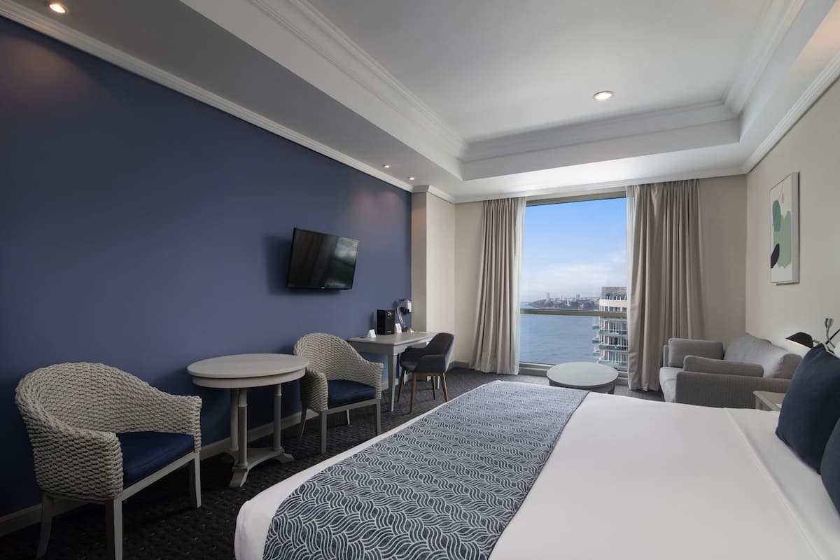 Une chambre d’hôtel avec un grand lit, un bureau, deux chaises, une télévision et une vue sur la ville.