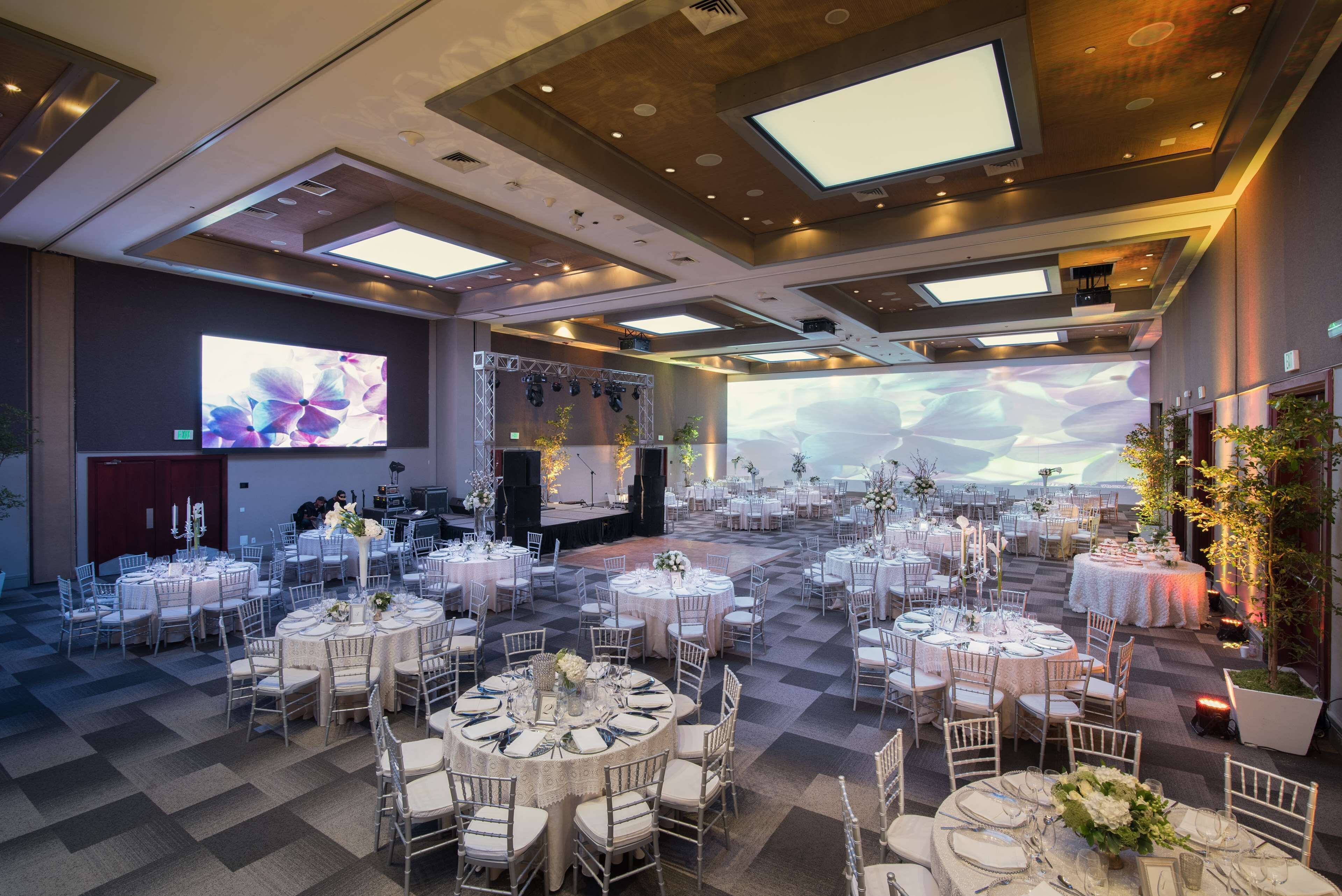 A spacious banquet hall with multiple round tables, each set with white tablecloths and chairs.
