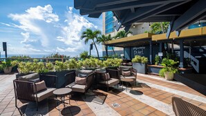 An outdoor seating area with multiple chairs and tables, surrounded by potted plants and a view of the ocean.