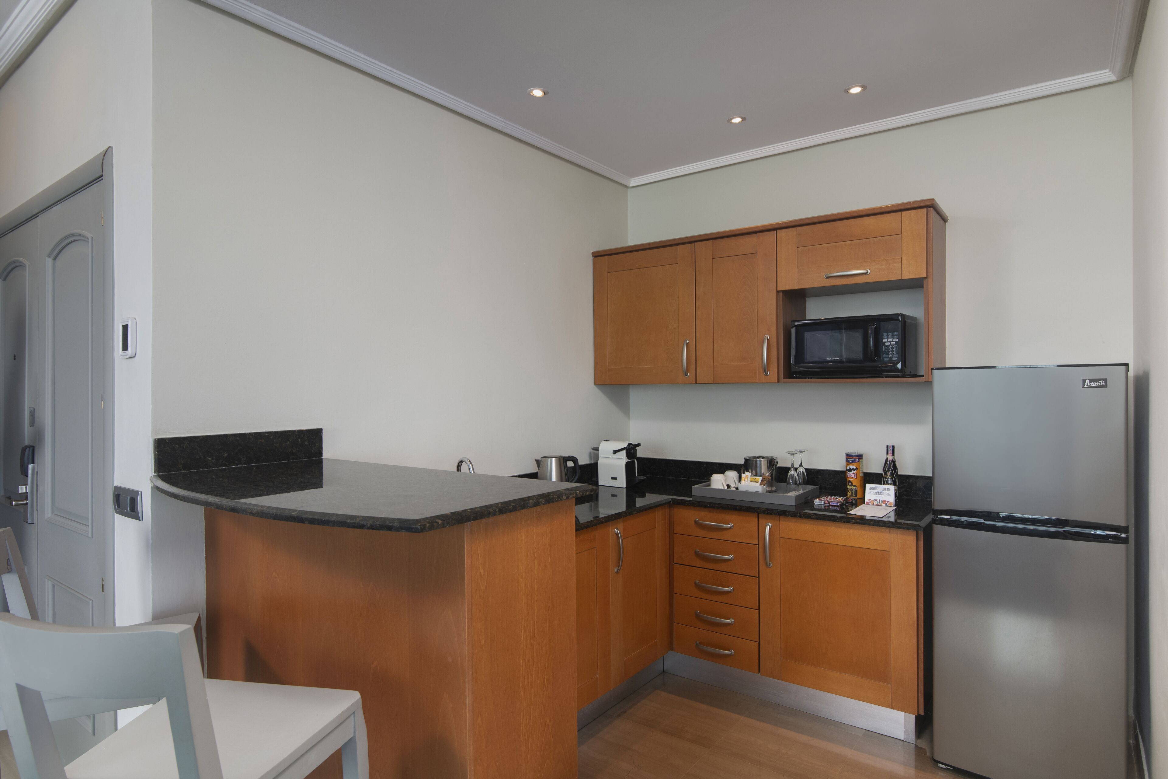A compact kitchen with wooden cabinets, a stainless steel refrigerator, and a black countertop.