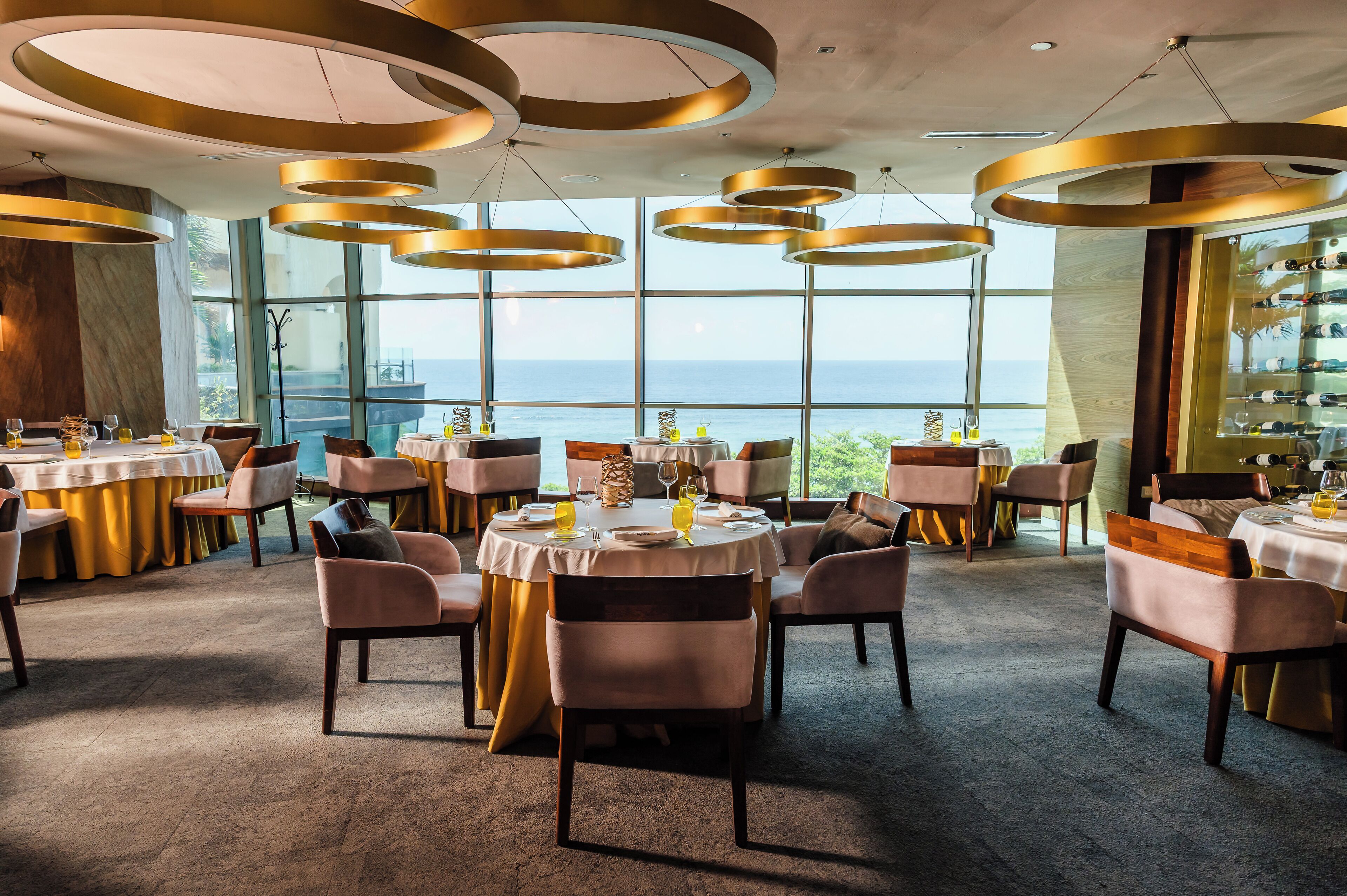 A restaurant with round tables, chairs, and a view of the sea.