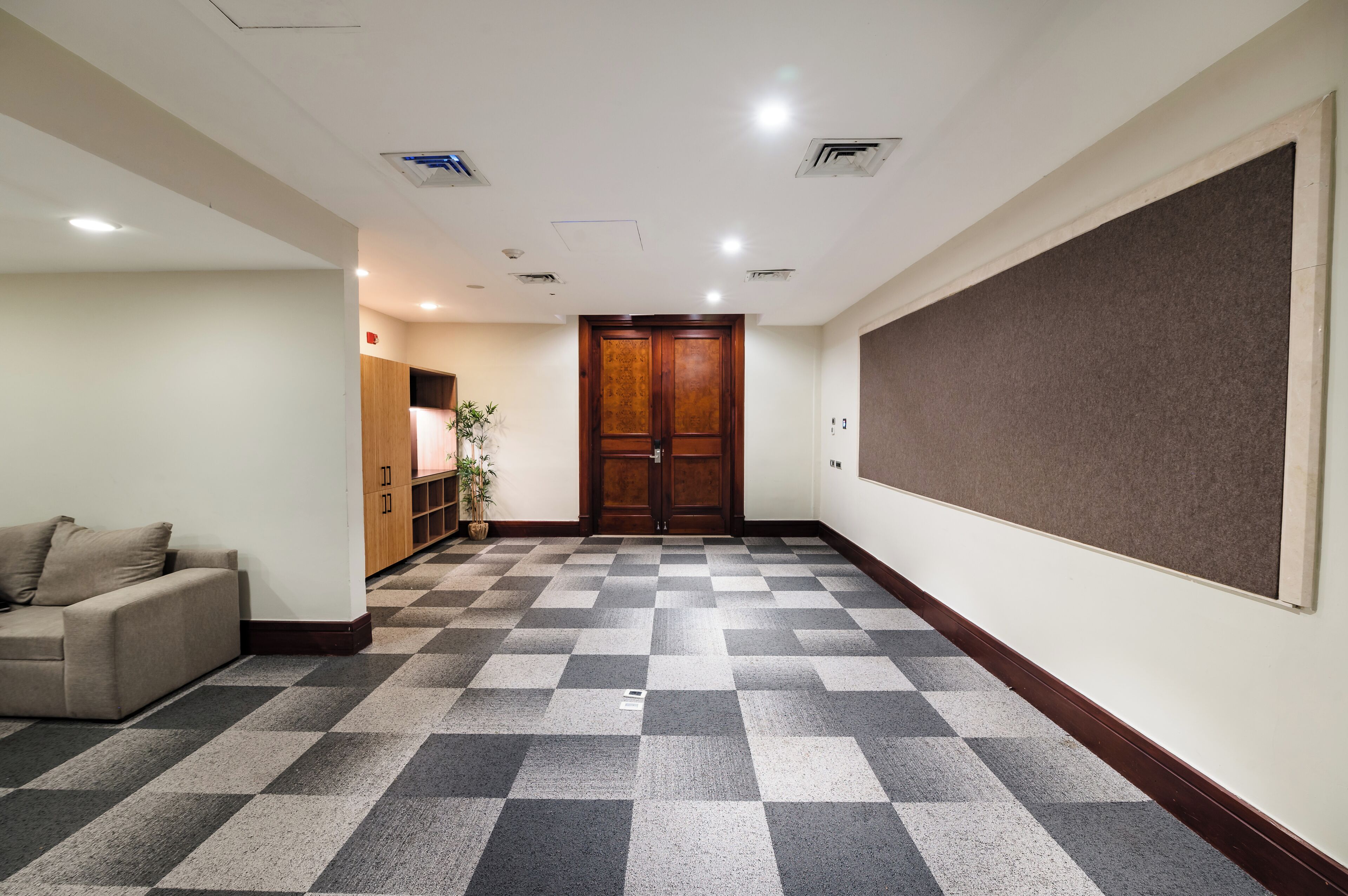 Un vestíbulo de hotel con piso a cuadros, una puerta de madera, una pizarra de anuncios y un sofá.