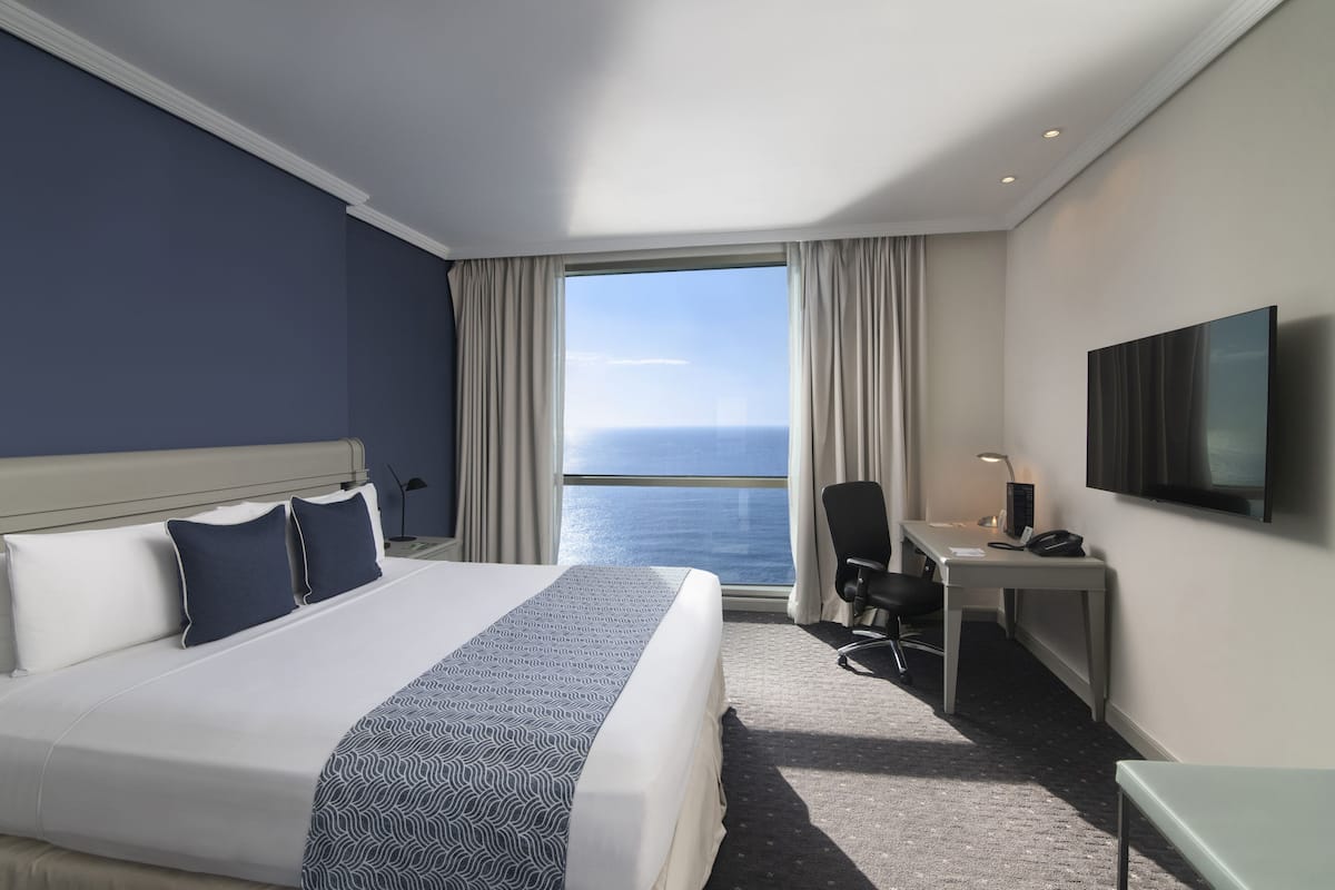 Une chambre d’hôtel avec un grand lit, un bureau, une chaise, une télévision et une vue sur l’océan.