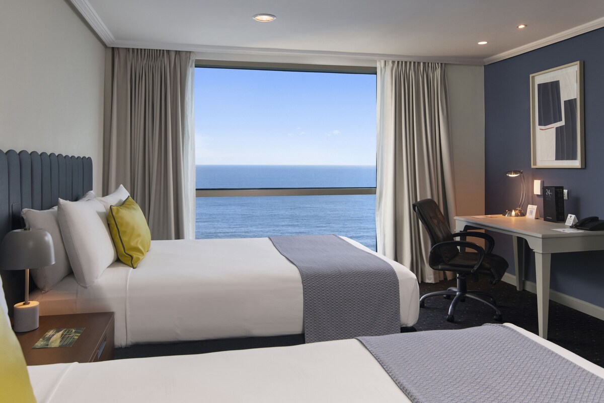 Une chambre d’hôtel avec un lit, un bureau, une chaise, une lampe et une vue sur la mer.