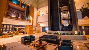 A spacious lobby with a high ceiling, a central staircase, and a seating area with sofas and chairs.