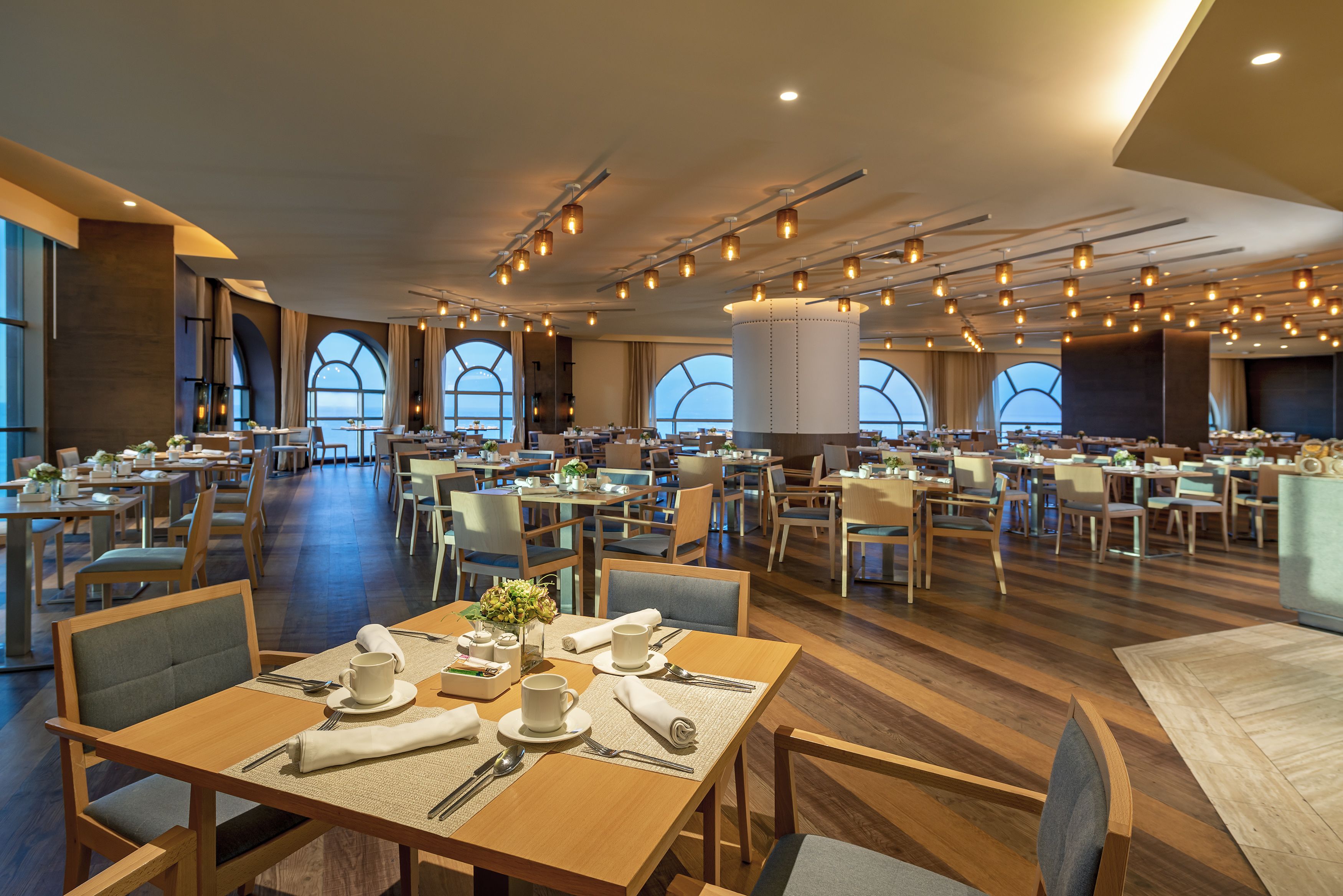 A spacious dining area with multiple tables and chairs, large windows, and modern lighting fixtures.
