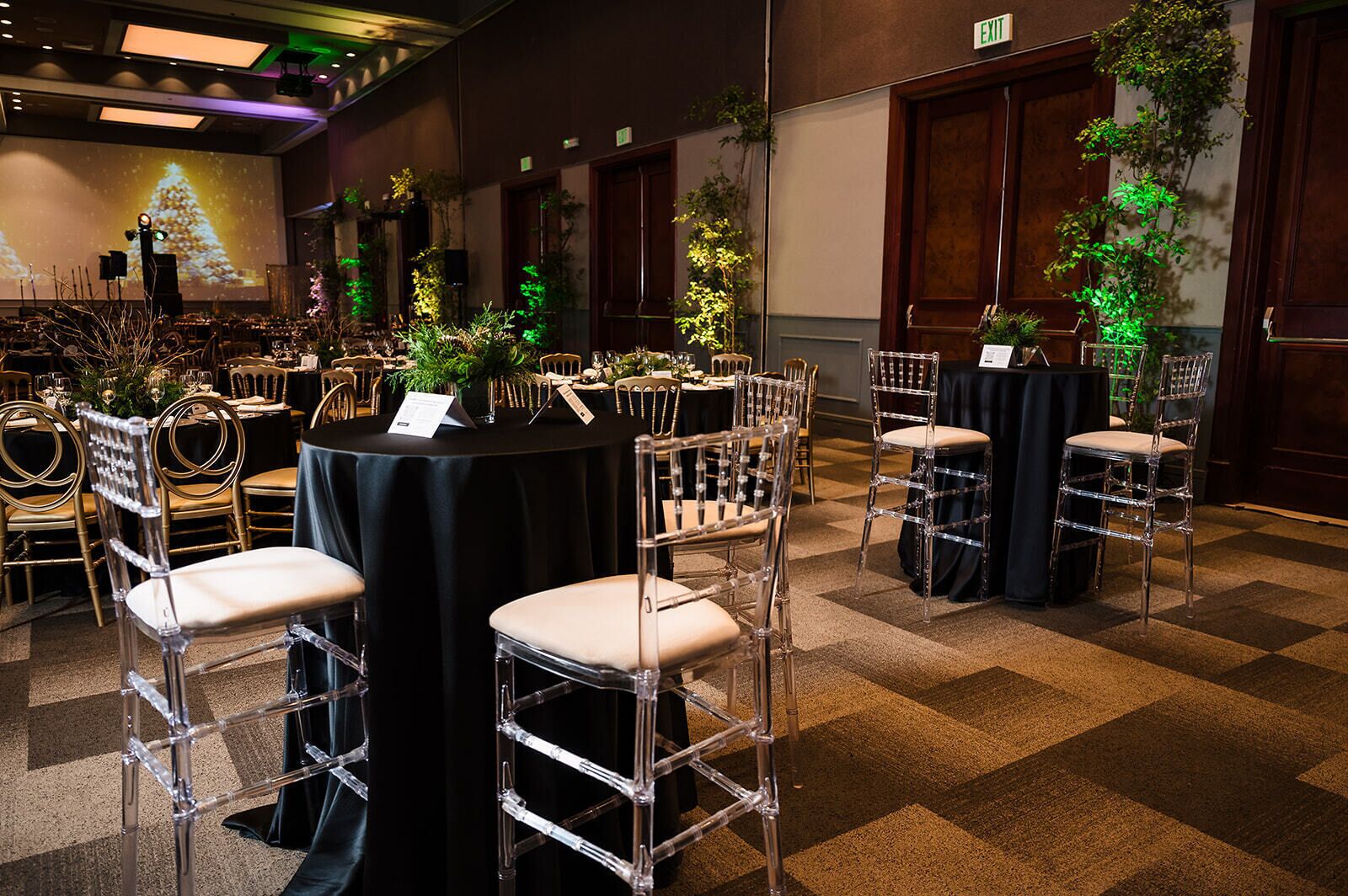 Une salle de banquet avec des tables rondes, des chaises transparentes et une scène sur laquelle est projetée une image d’un sapin de Noël.